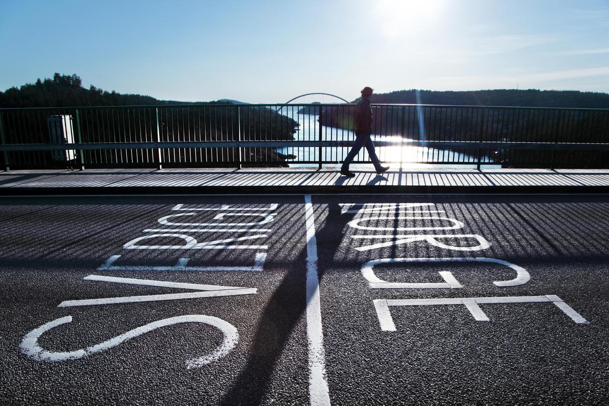 A person walking across the bridge on the border of Sweden and Norway. Sun is shining and a river flows beneath.